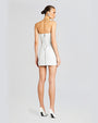 A backside full body view of a brunette model with her hair tied back, wearing a strapless white mini dress with an open back and a zipper down the back. The model is also wearing a white pointed-toe heels with a white background.