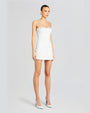 A full body view of a brunette model with her hair tied back, wearing a strapless white mini dress with a straight neckline and a straight lacey neckline. The model is also wearing white pointed-toe heels and standing against a white background.