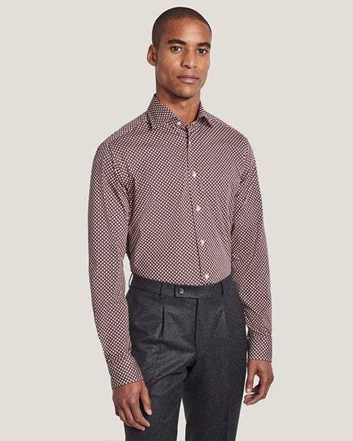 A knee-up view of a model wearing a red and white spotted button up shirt tucked into grey trousers, standing in front of a white background.