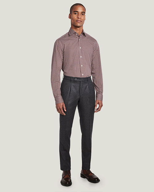 An angled full body view of a model wearing a red and white patterned button up shirt tucked into gray trousers and brown dress shoes. The background is plain white.