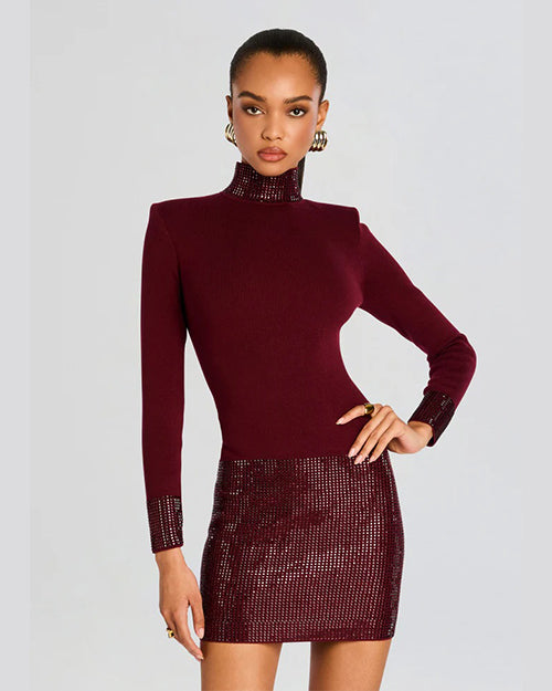 A knee-up view of a model wearing thick silver hoop earrings, a dark red dress with long sleeves, a high neckline, and a shiny texture on the skirt, cuffs, and neck. The background is plain white.