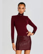 A knee-up view of a model wearing thick silver hoop earrings, a dark red dress with long sleeves, a high neckline, and a shiny texture on the skirt, cuffs, and neck. The background is plain white.