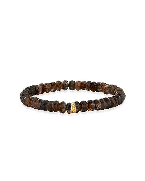 A brown textured beaded bracelet with a gold ring detail adorned with gems in the center. The background is plain white.
