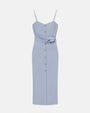 A light blue dress with thin straps behind a white background. The dress has buttons running down the front and light blue fabric tied around the waist, and a seam down the center.