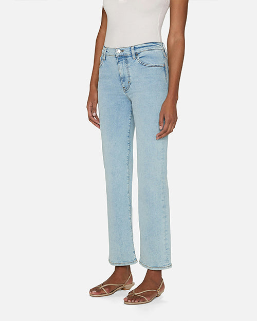 A side view of person wearing light blue jeans and a white sleeveless top tucked in. The jeans are high-waisted with front pockets and straight legs. The pants have button and zipper closure. The person is also wearing open-toe sandals.