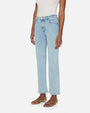 A side view of person wearing light blue jeans and a white sleeveless top tucked in. The jeans are high-waisted with front pockets and straight legs. The pants have button and zipper closure. The person is also wearing open-toe sandals.