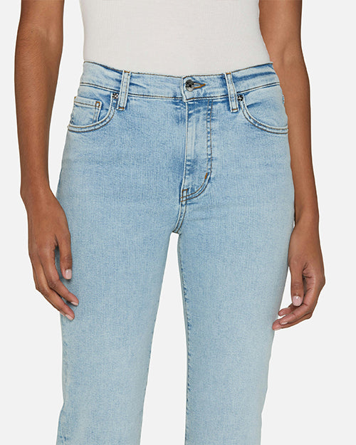 A close-up thigh level view of a person wearing light blue jeans and a white sleeveless top tucked in. The jeans are high-waisted with front pockets and straight legs. The pants have button and zipper closure.