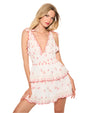 A knee-up view of a blonde model with her hand on her knee wearing a white sleeveless dress with a V-neck, red cherry patterns, red scalloped edges, and a double layered skirt. The background is plain white.