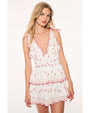 A knee-up view of a blonde model wearing a white sleeveless dress with a V-neck, red cherry patterns, red scalloped edges, and a double layered skirt. The background is plain white.