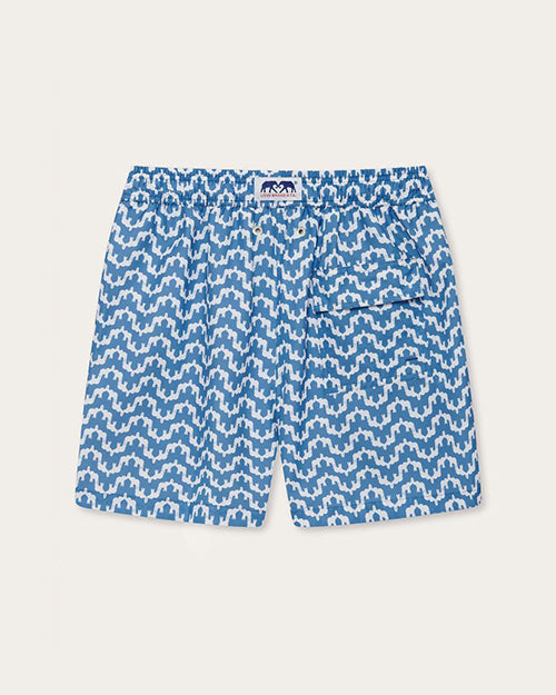 An inside out pair of blue and white zigzag patterned swim shorts with missing drawstrings, and a white tag on the waistline featuring two blue elephants. The background is white.