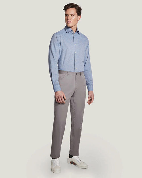 An angled full body view of a model wearing a light-blue button up shirt tucked into gray buttoned pants and white sneakers, standing in front of a white background.