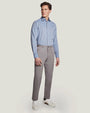 An angled full body view of a model wearing a light-blue button up shirt tucked into gray buttoned pants and white sneakers, standing in front of a white background.