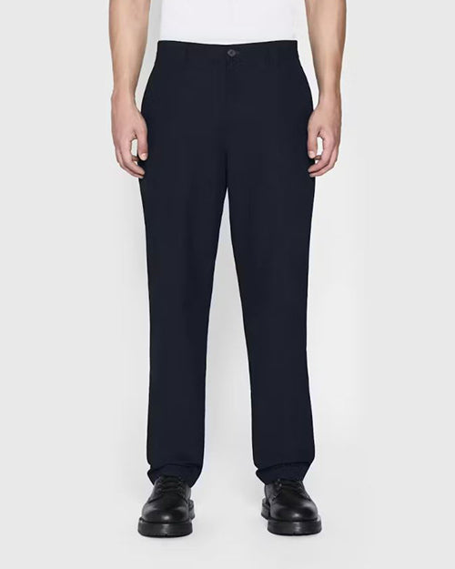 A lower body view of a model wearing a white shirt tucked into navy trousers, and black dress shoes. The background is plain and light-colored.