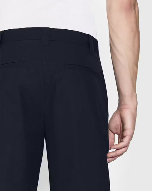 A close-up backside view of a models' hip, wearing a white shirt tucked into navy trousers, and black dress shoes. The background is plain and light-colored.
