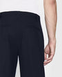 A close-up backside view of a models' hip, wearing a white shirt tucked into navy trousers, and black dress shoes. The background is plain and light-colored.