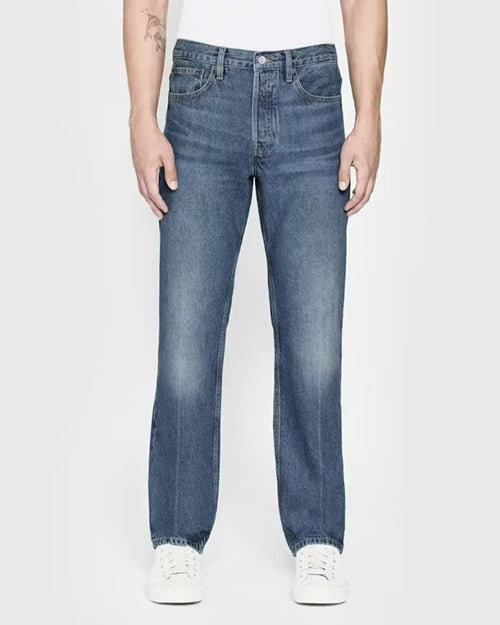A lower-body view of a model wearing blue jeans with a faded look tucked into a white t-shirt and sneakers. The background is completely white.