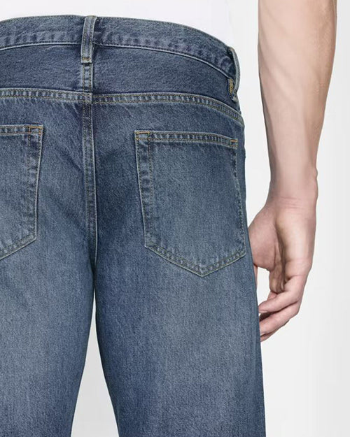 A backside waist level view of a model wearing blue jeans tucked into a white shirt. The background is plain white.