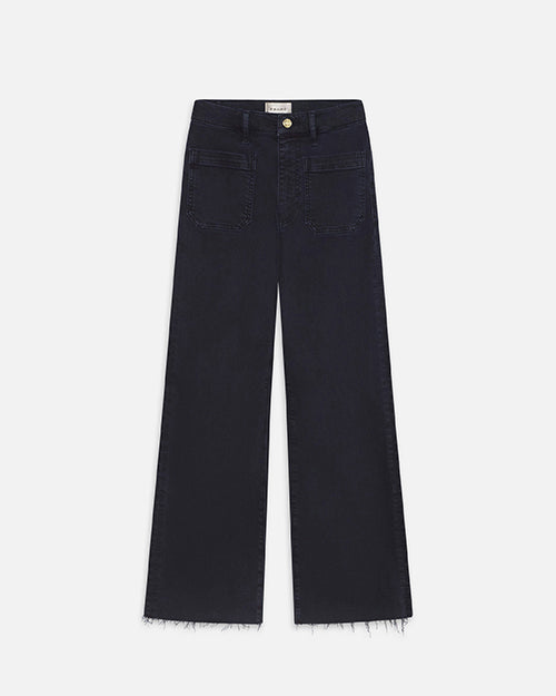 A full shot of a pair of navy denim jeans with a gold button and frayed hems in front of a white background.
