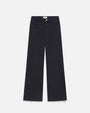 A full shot of a pair of navy denim jeans with a gold button and frayed hems in front of a white background.