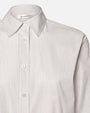 A close-up shoulder level image of a white long-sleeve button-up shirt with a collar. The shirt has thin vertical stripes and white buttons. The inside neckline contains a tag that reads "FRAME".