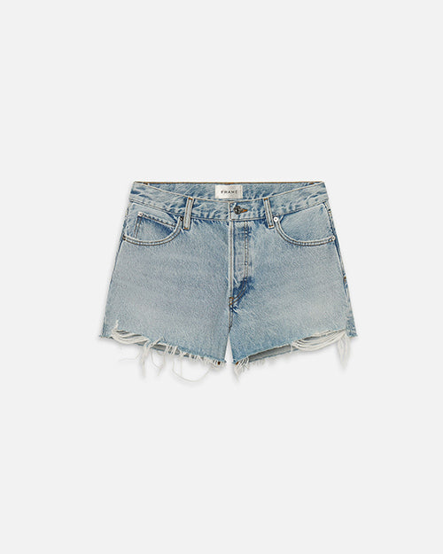 A pair of light-wash denim shorts with frayed ends sitting in front of a white background. The inner waistline has a rectangular white tag with the word "FRAME" on it.
