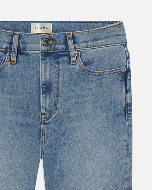 A close-up view of the waistline of a pair of blue denim jeans. The jeans have zipper and button closure, with a rectangular white tag reading "FRAME" at the inner waistline.