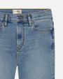 A close-up view of the waistline of a pair of blue denim jeans. The jeans have zipper and button closure, with a rectangular white tag reading "FRAME" at the inner waistline.
