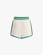 The backside view of a pair of white athletic style shorts with green trim along the sides and hem. The shorts have an elastic waistband with 2 green stripes and have a relaxed fit. The background is white.