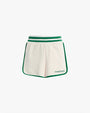 The frontside view of a pair of white athletic style shorts with green trim along the sides and hem. The shorts have an elastic waistband with 2 green stripes, and the bottom left leg reads "Favorite Daughter" in green text.