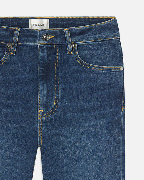 A close-up view of a pair of blue jeans with classic gold stitching. The inner tag reads "FRAME".