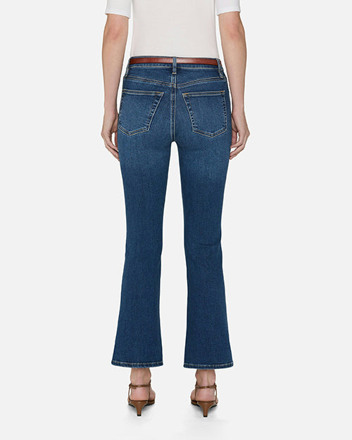 A backside, lower body view of a model wearing blue jeans with a slight flare at the end, a tucked in white top, and brown sandals. She is standing in front of a white background.