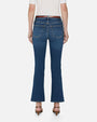 A backside, lower body view of a model wearing blue jeans with a slight flare at the end, a tucked in white top, and brown sandals. She is standing in front of a white background.