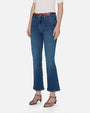An angled, lower body view of a model wearing blue jeans with a slight flare at the end, a tucked in white top, and a brown belt and sandals. She is standing in front of a white background.