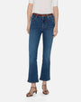 A lower body view of a model wearing blue jeans with a slight flare at the end, a tucked in white top, and a brown belt and sandals. She is standing in front of a white background.