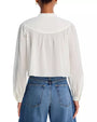 A torso level, backside view of a brunette model wearing a white long-sleeve blouse with a high collar and button-down front, with a yoke design at the shoulders and loose-fitting sleeves that gather at the cuffs. The person is also wearing blue jeans and standing in front of a white background.