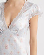 A close-up chest level view of a model wearing a light-blue dress featuring short sleeves with lacey edging and a laced V-neckline. The dress has a floral pattern with small pink flowers scattered throughout the fabric and a stitched waistline.