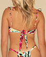 The backside view of a blonde model wearing a thin strapped bandeau style bikini top with a colorful floral brushstroke pattern. The top is tied in the back, and the model is wearing matching high waisted bottoms. The background is white.