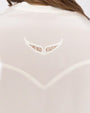 A close-up of a models' back of a white shirt with a small lace detail in the shape of wings above a V-shaped linear detail.