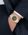 Gold and silver watch on a person's wrist with a dark suit and white shirt.