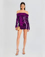 A full body shot of a dark-haired model wearing a purple sparkly off-the-shoulder dress with long sleeves. The model is accessorizing with a metallic gold clutch, gold earrings and pink high heels. The background is plain white.
