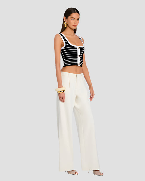 Woman wearing a black and white striped top and white pants on a light gray background