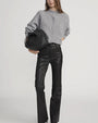Person wearing a light gray button-up cardigan with a round neckline, paired with high-waisted black leather pants and holding a large black handbag.