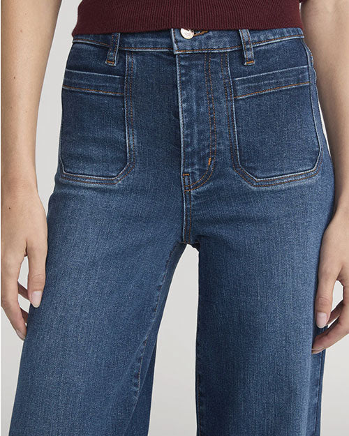 Close-up of high-waisted blue wide-leg jeans with front patch pockets and button closure, paired with a burgundy knit top.