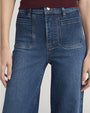 Close-up of high-waisted blue wide-leg jeans with front patch pockets and button closure, paired with a burgundy knit top.