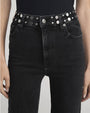 Close-up of high-waisted black jeans paired with a black belt featuring silver studs and a round metal buckle.