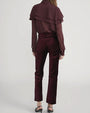 Back view of high-waisted velvet pants in deep burgundy paired with a long-sleeve button-up blouse featuring layered ruffle details.