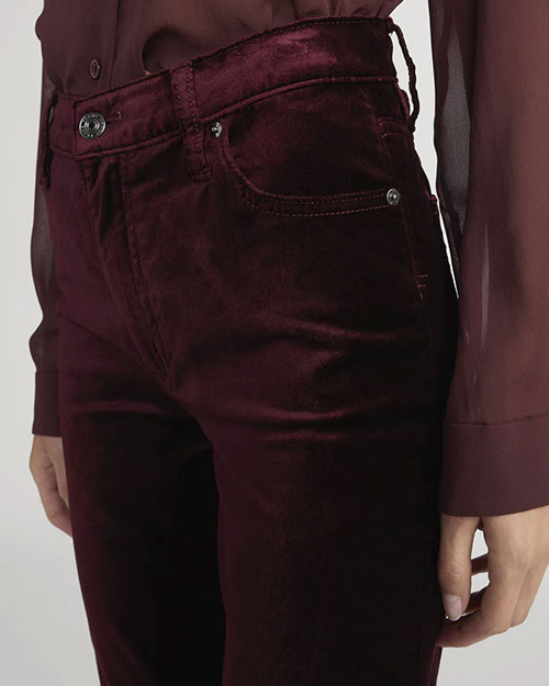Close-up of high-waisted velvet pants in deep burgundy with front pockets and button closure, paired with a sheer long-sleeve blouse in a matching shade.
