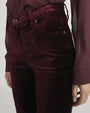 Close-up of high-waisted velvet pants in deep burgundy with front pockets and button closure, paired with a sheer long-sleeve blouse in a matching shade.