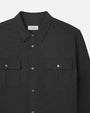 A close-up view of a dark long-sleeve silver button-up shirt with two chest pockets, and a rectangular white tag with the brand name "FRAME" on it. The background is plain white.