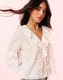 A waist-up frontal view of a brunette model with white blouse featuring ruffled detailing down the front, long sleeves, vertical lace detailing on the torso, and horizontal detailing on the arms.